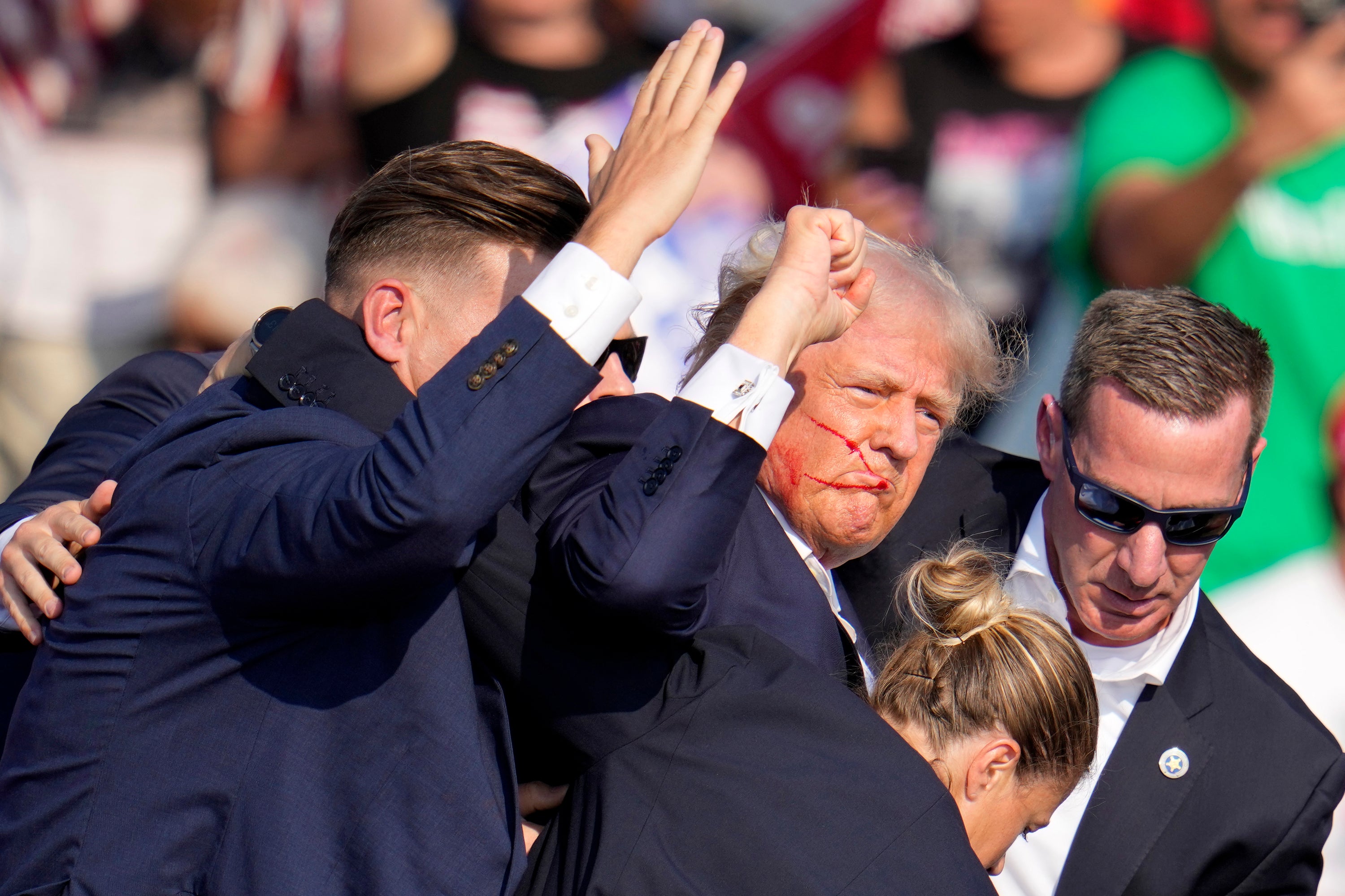 Donald Trump raises his fist as he is helped off the stage by Secret Service agents