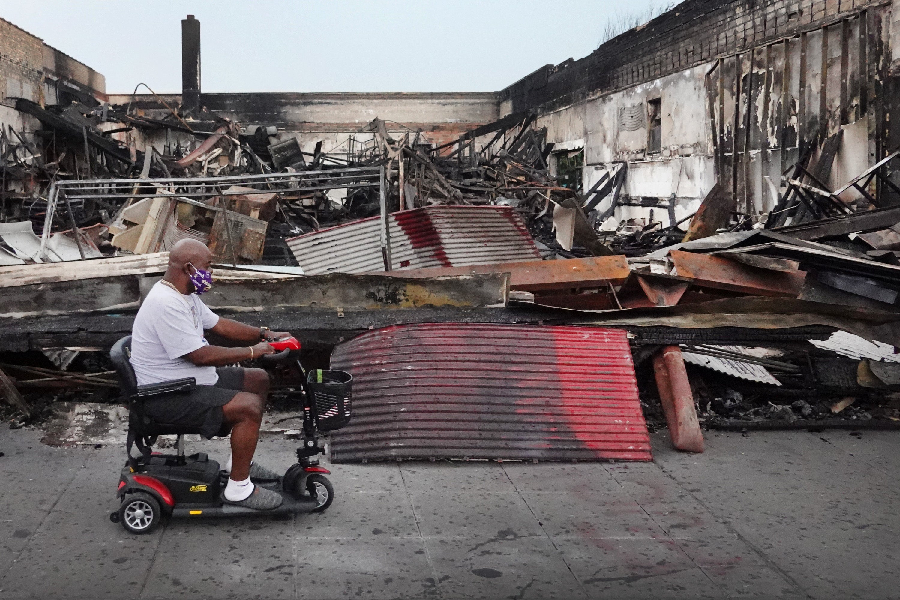 A man rides a scooter past the charred wreckage of a building after being burned to the ground during last week’s rioting sparked by the death of George Floyd on June 2, 2020 in Minneapolis, Minnesota