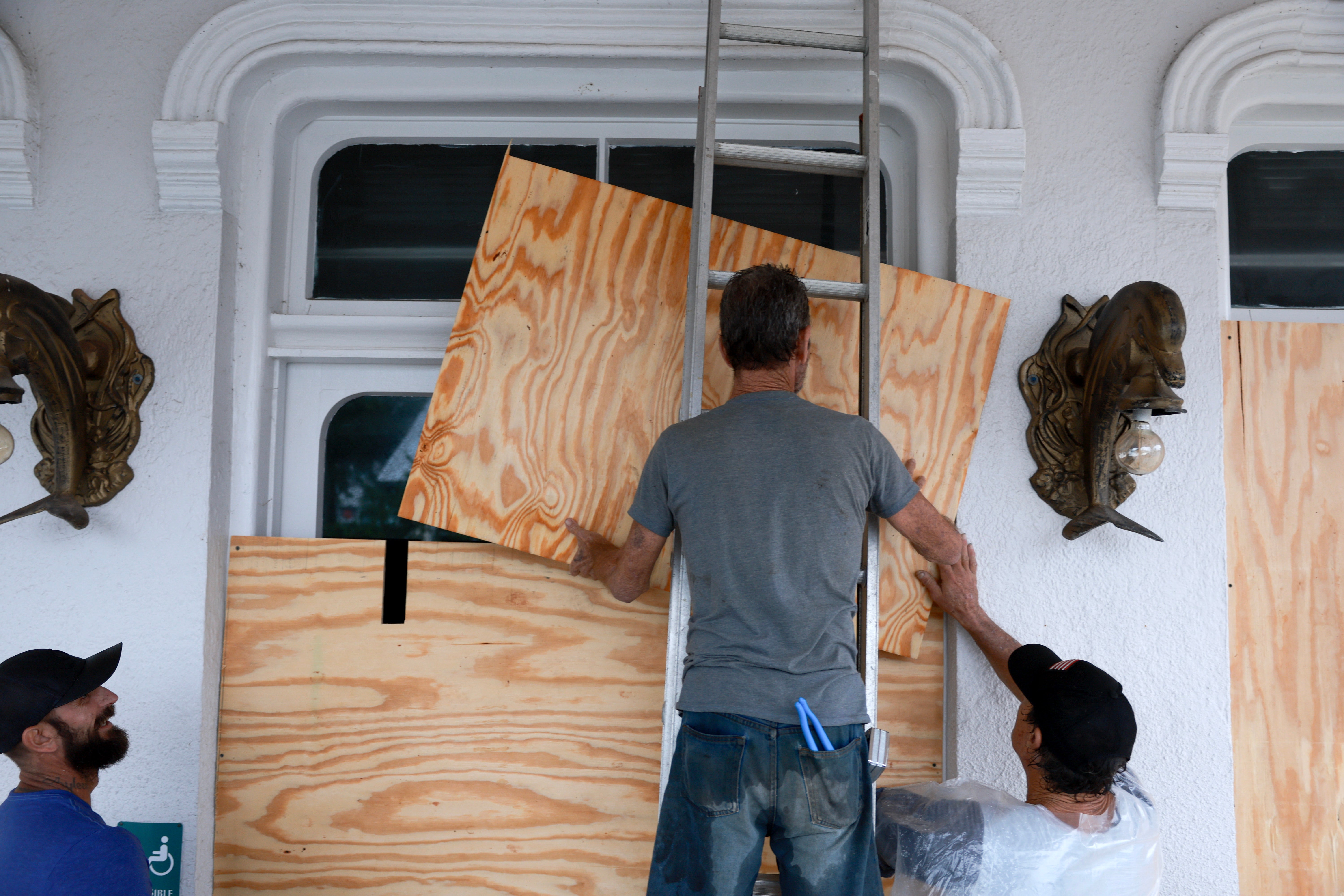 Workers place plywood over the windows of a business as they prepare for the arrival of Hurricane Debby, which has strengthened as it moves through the Gulf of Mexico in Cedar Key, Florida