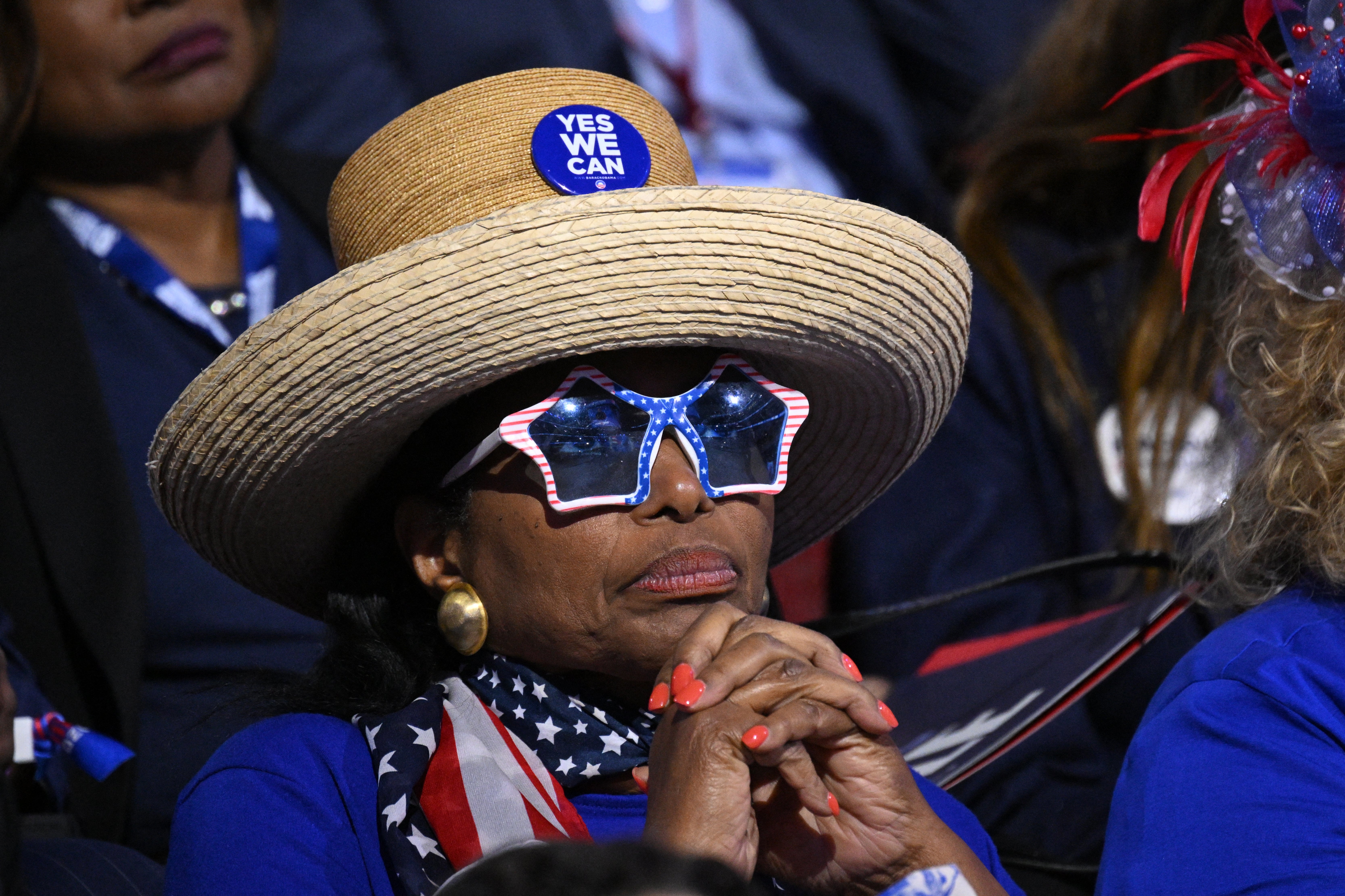 A delegate dressed in red, white and blue intensely listens to a speaker on the second day of the DNC while also wearing a straw hat and star-shaped sunglasses