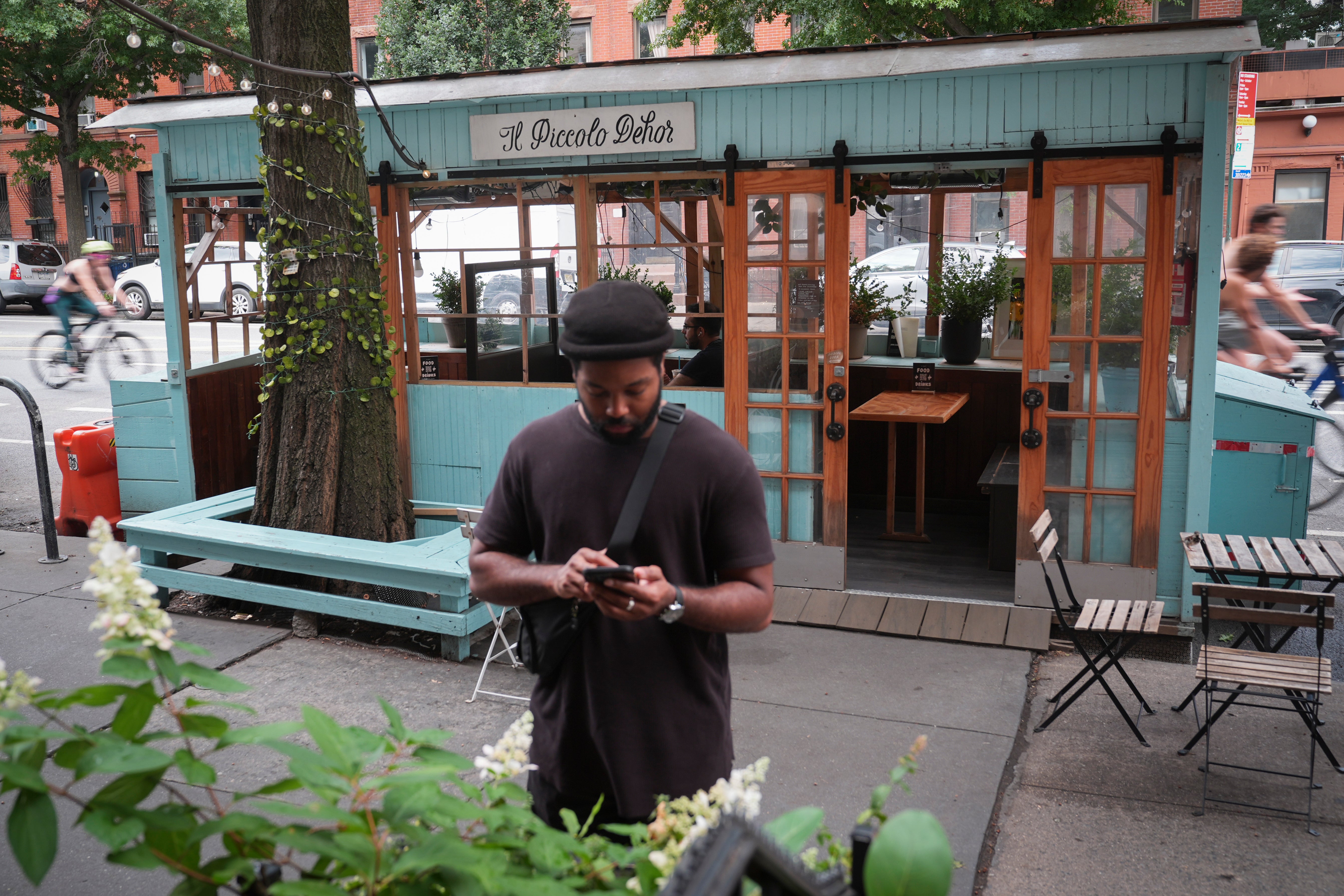 A pedestrian stops on the sidewalk beside the outdoor dining shed at Caffe de Martini, Wednesday, July 31, 2024, in the Brooklyn borough of New York. New outdoor dining regulations that will see many of the street and sidewalk enclosures disappear went into effect in New York City on August 3, 2024