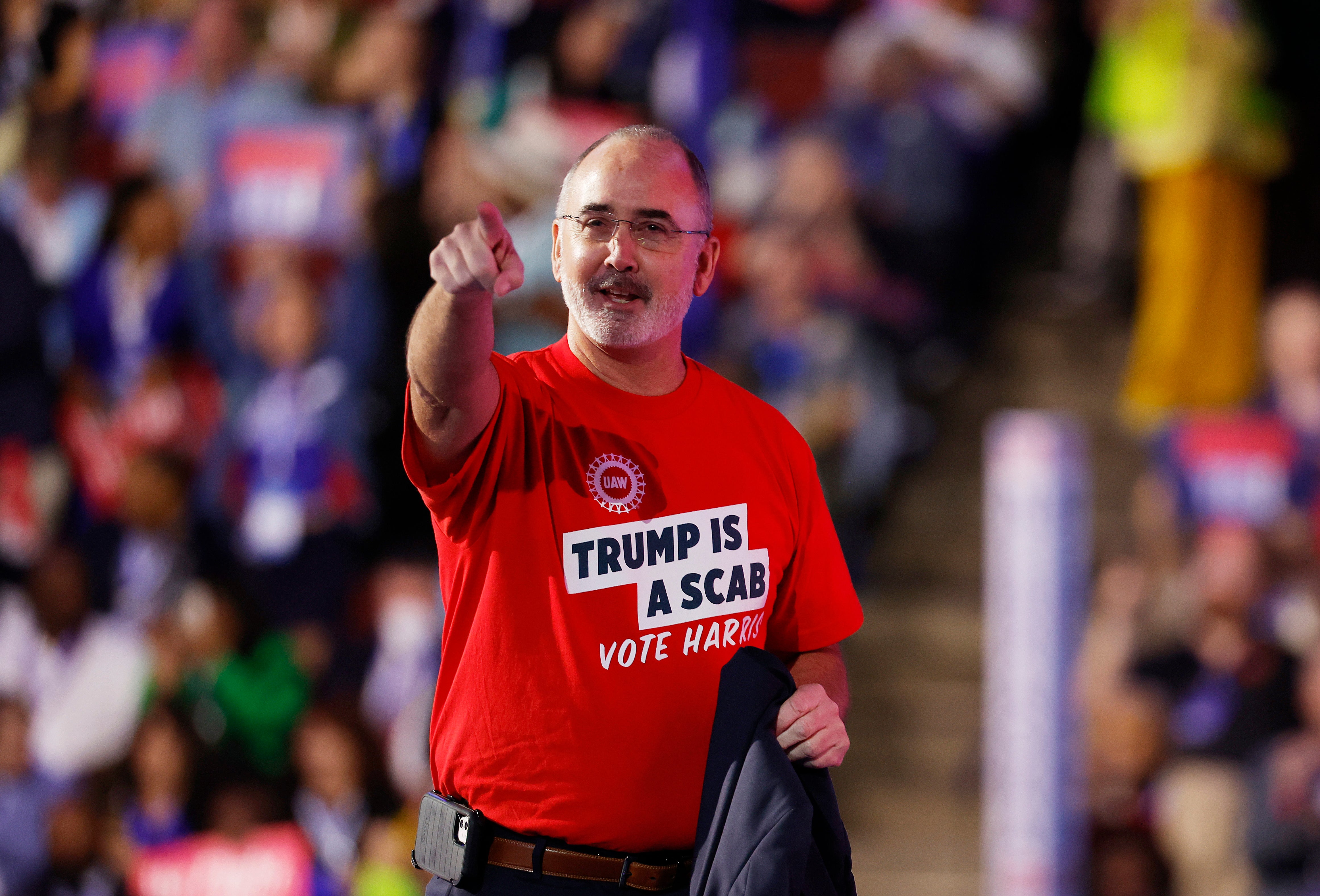 United Auto Workers President Shawn Fain unveils his belt phone holster. Also wearing ‘Trump is a scab, vote Harris’ t-shirt.