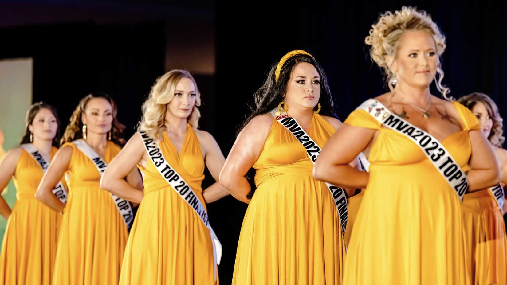 Ms. Veteran America 2023 finalists line up in yellow dresses and white finalist sashes, with their hands behind their backs.